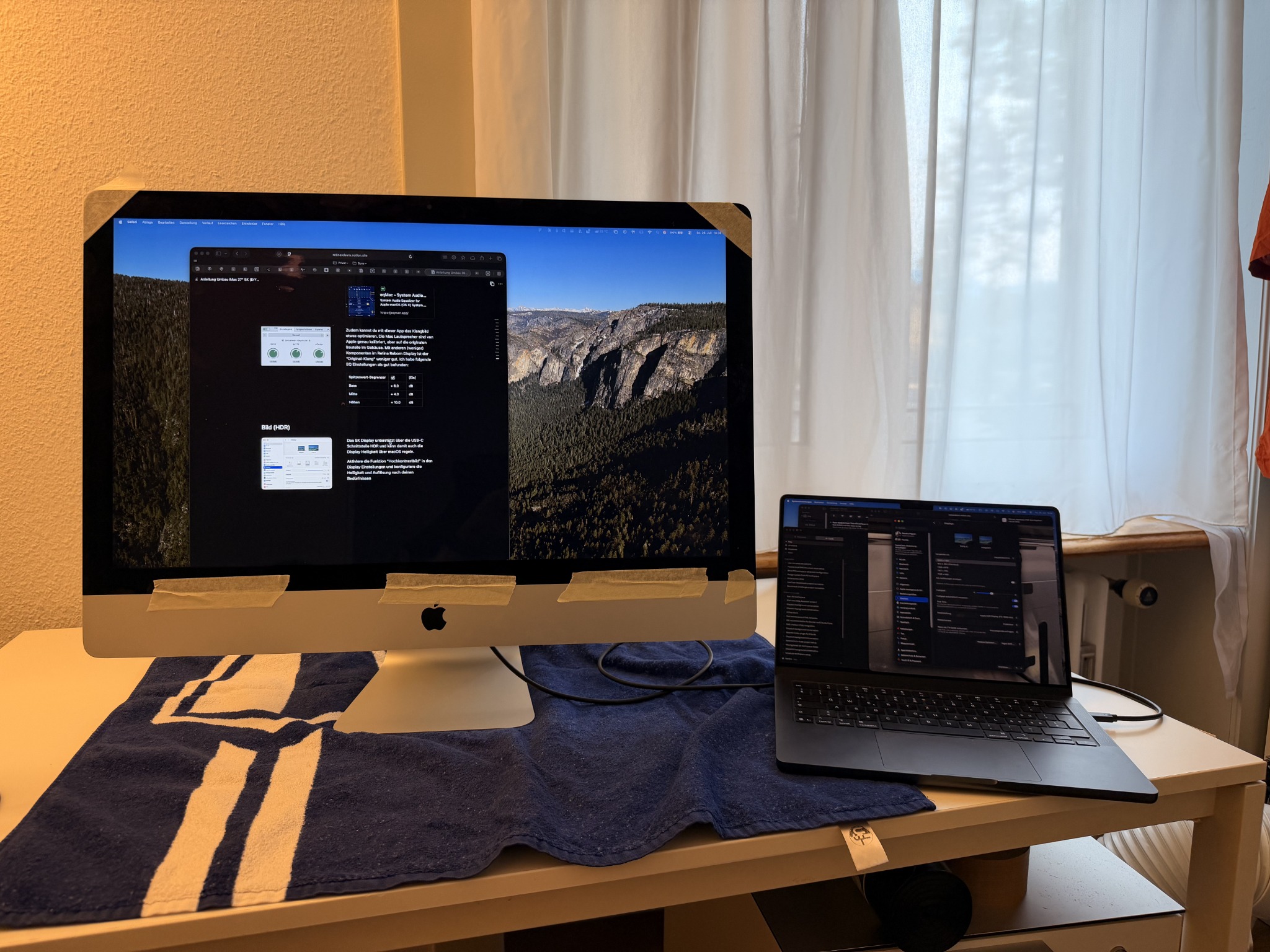 iMac-Display in Betrieb neben einem geöffneten MacBook auf dem Arbeitstisch.