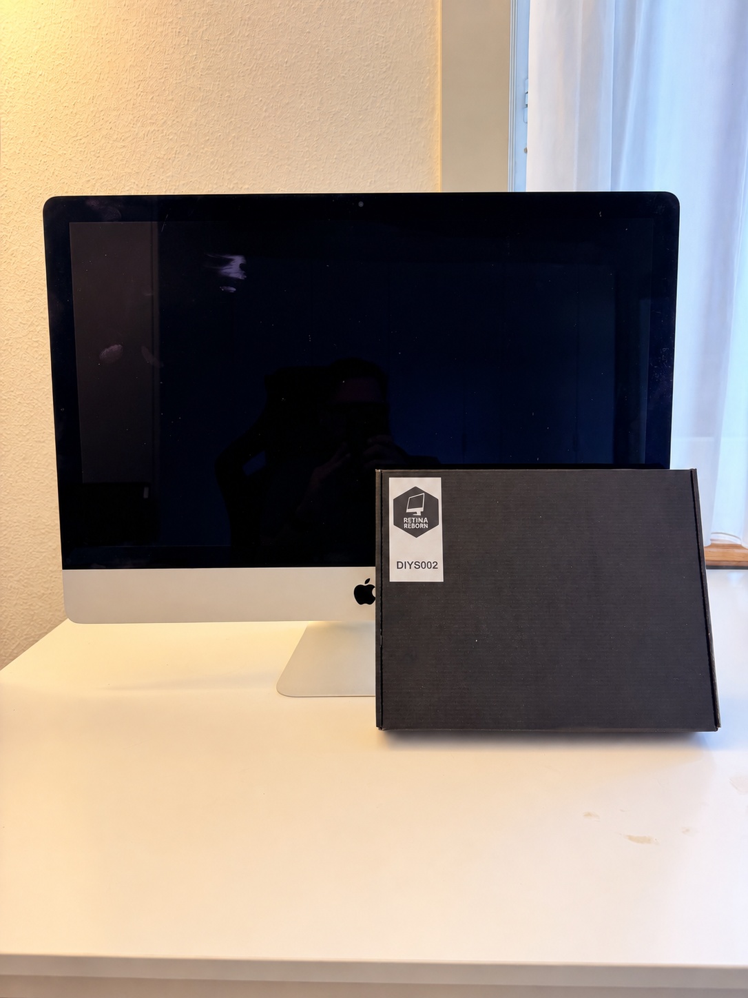 Geschlossener iMac mit der Verpackung des Umbau-Sets auf dem Tisch.